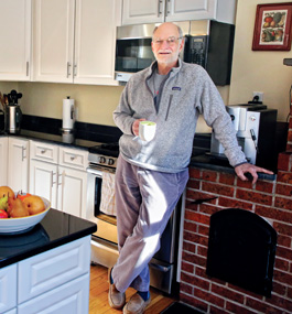 Michael Rosbash leans against a counter in his kitchen, holding a mug.